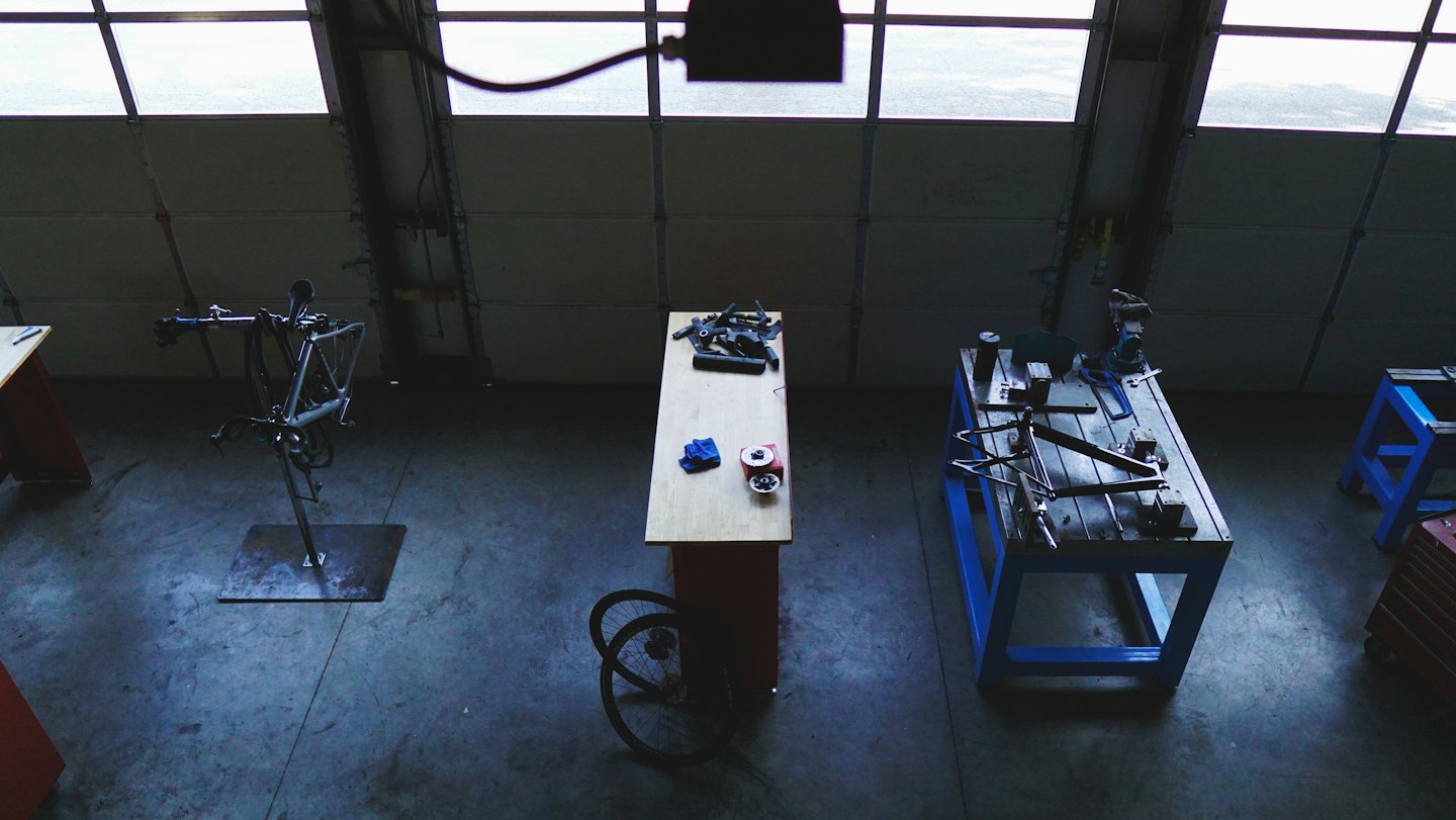 Officina di riparazione biciclette con banchi da lavoro, attrezzi e pezzi di ricambio.