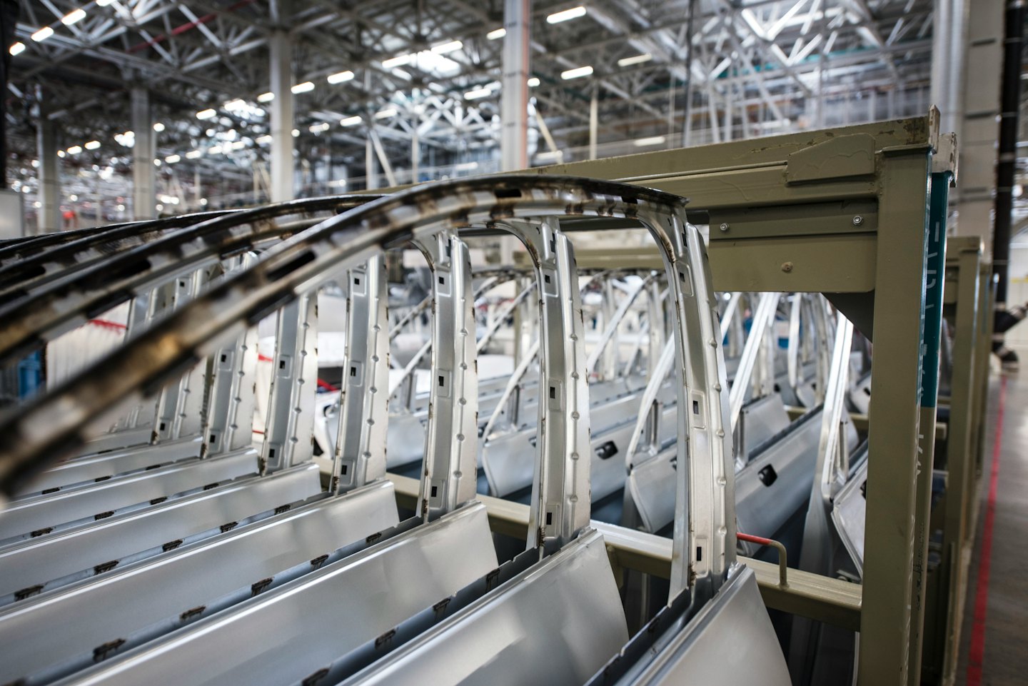 Telai di portiere d'auto in metallo grezzo impilati su scaffalature industriali in una fabbrica.